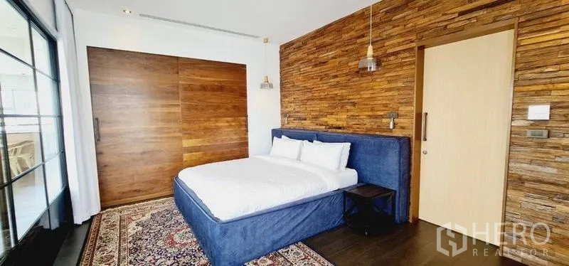 Condominium for rent in Watthana, Bangkok - Bedroom with textured wood accent wall, sliding timber door, upholstered bed and rug.
