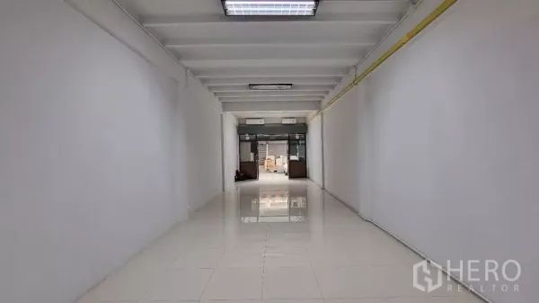 Townhouse for rent in Huai Khwang, Bangkok - Long open-plan ground floor with glossy white tiles and a glass frontage.