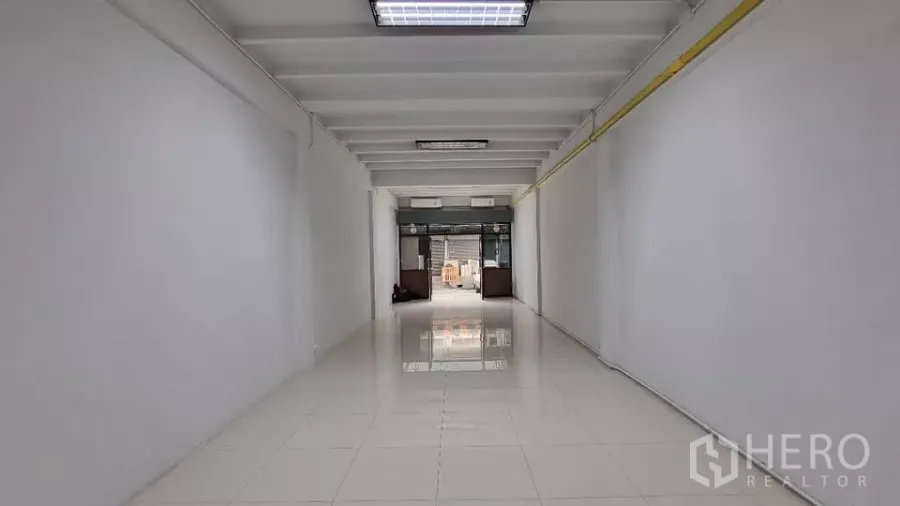 Townhouse for rent in Huai Khwang, Bangkok - Long open-plan ground floor with glossy white tiles and a glass frontage.