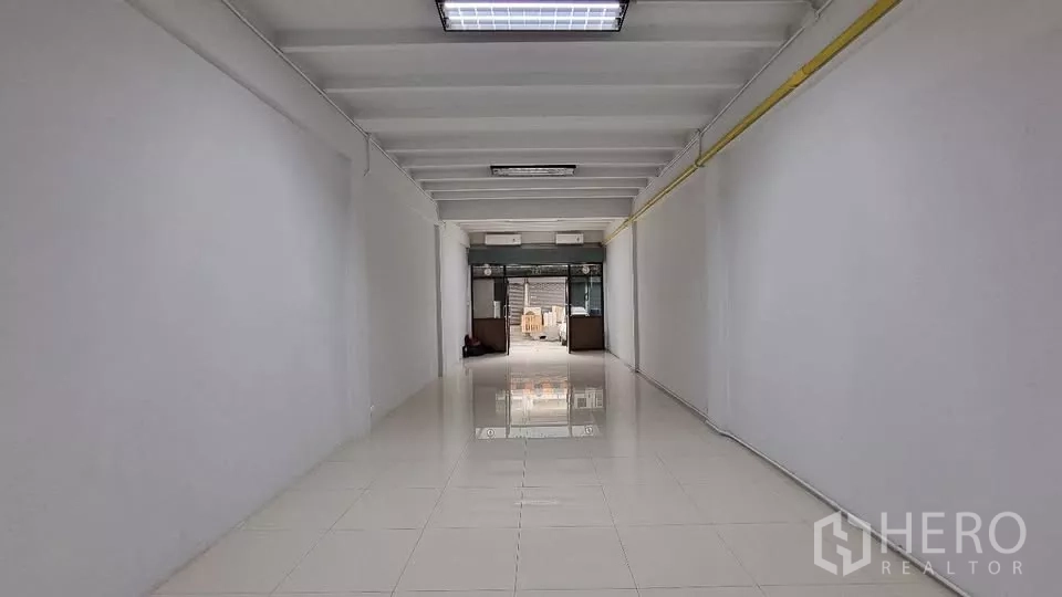 Townhouse for rent in Huai Khwang, Bangkok - Long open-plan ground floor with glossy white tiles and a glass frontage.