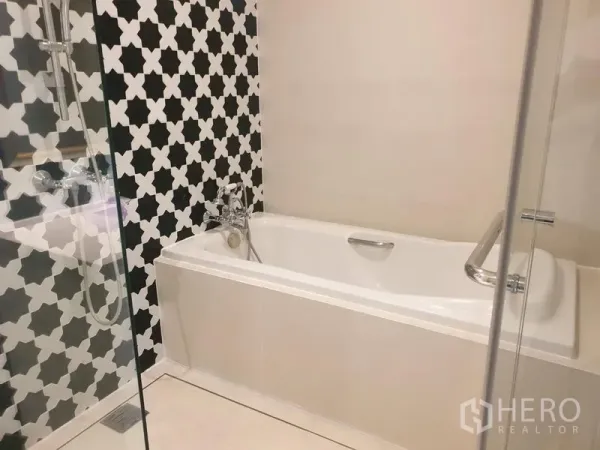 Condominium for rent in Khlong Toei, Bangkok - Modern bathroom featuring a glass shower and bathtub against black-and-white patterned tiles.