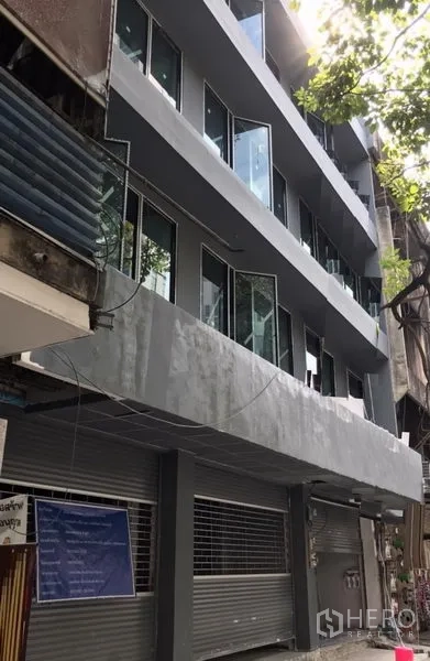 Shophouse for rent in Khlong Toei, Bangkok - Newly renovated multi-storey shophouse facade with grey exterior, glass windows and ground-floor roller shutters on a tree-lined Sukhumvit lane.