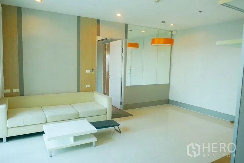 Condominium for rent or sale in Khlong San, Bangkok - Light-filled living room with cream sofa, coffee table and mirrored feature wall.