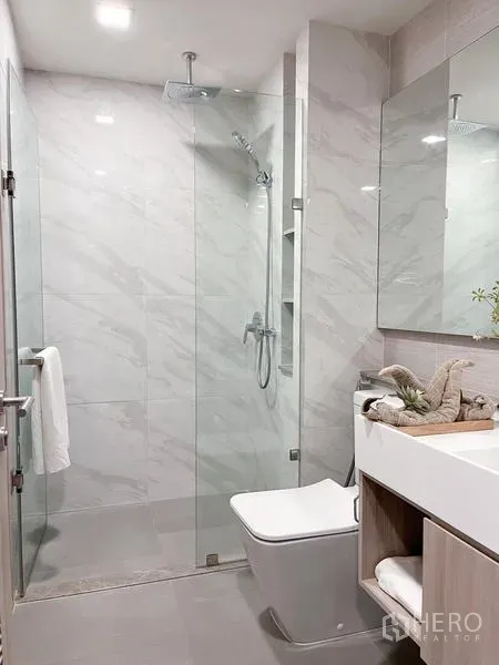Condominium for rent in Watthana, Bangkok - Bright bathroom featuring a glass-enclosed shower, wall-hung toilet, and marble-effect tiles.