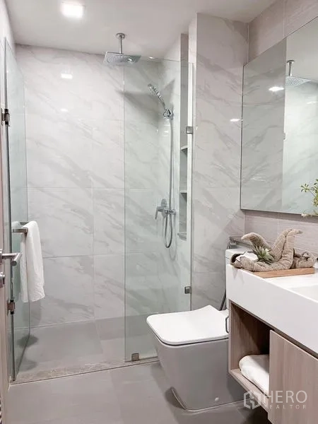 Condominium for rent in Watthana, Bangkok - Bright bathroom featuring a glass-enclosed shower, wall-hung toilet, and marble-effect tiles.