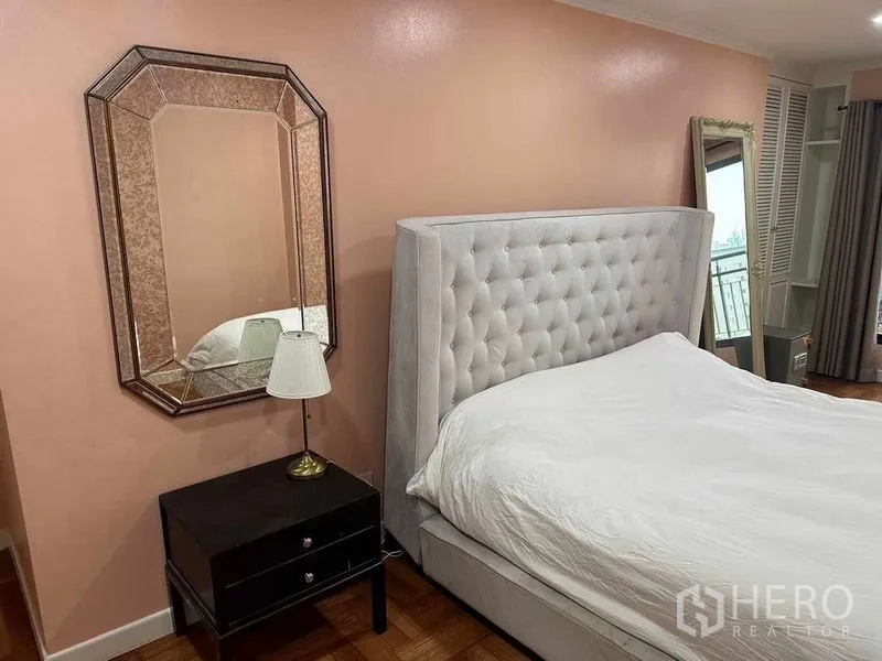Condominium for sale in Bangkok - Close view of the primary bedroom with mirrored wall decor, bedside table and padded headboard.