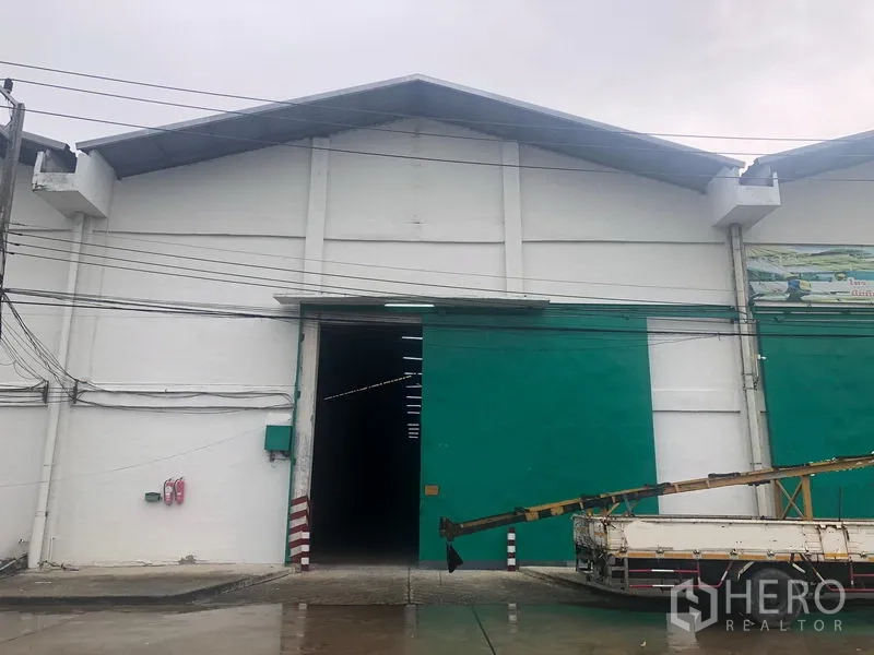 Warehouse for rent in Pathum Thani - Front facade of a large white warehouse with a green sliding door and truck access.