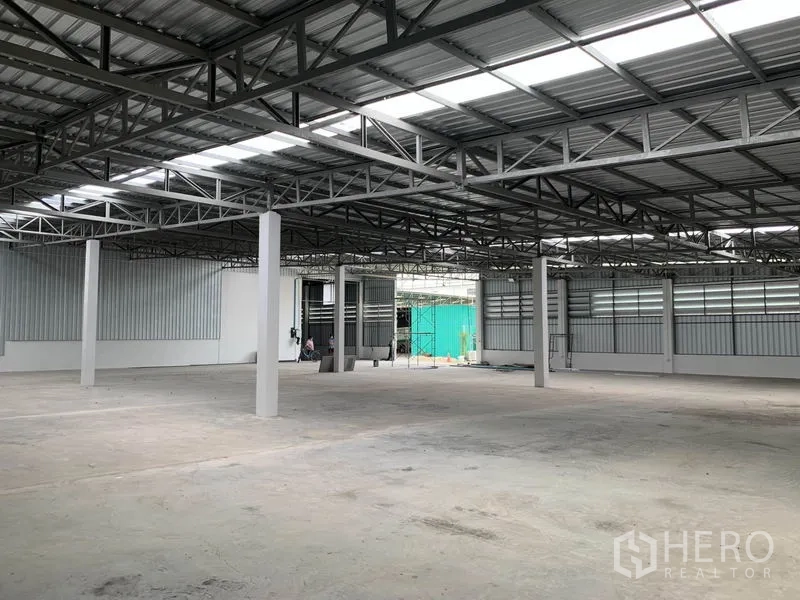 Warehouse for rent in Mueang Pathum Thani, Pathum Thani - Open-plan storage space with high ceiling, concrete flooring and large roller doors for loading.