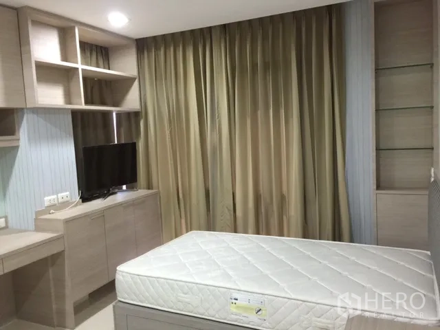 Condominium for rent or sale in Khlong Toei, Bangkok - Bedroom with built-in cabinetry, desk, TV and floor-to-ceiling curtains.