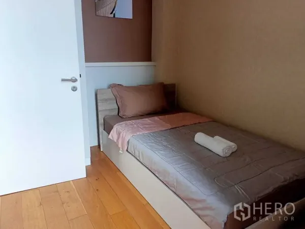 公寓 出租在Watthana, Bangkok - 温馨次卧，木地板与中性色墙面，整洁单人床在白色门旁。