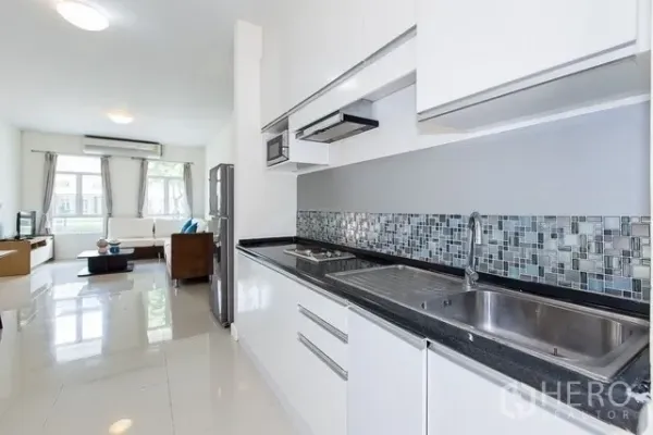 Townhouse for rent in Watthana, Bangkok - Sleek galley kitchen with white cabinetry, mosaic backsplash, double sink and view to living area.