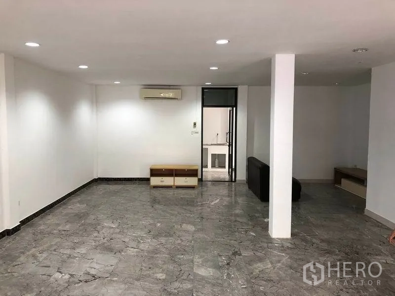 Townhouse for rent in Watthana, Bangkok - Spacious living room with central column, recessed lights, air conditioner and doorway to the kitchen.