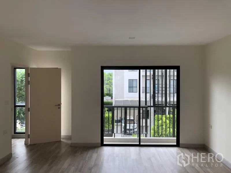 Townhouse for rent or sale in Saphan Sung, Bangkok - Bedroom with large sliding doors to a balcony overlooking the townhouse community greenery.