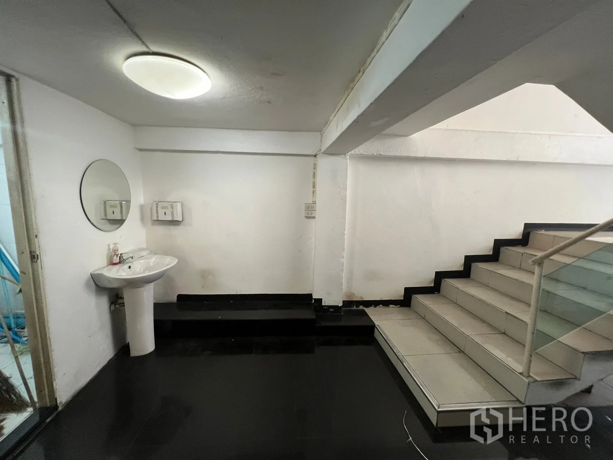 Shophouse for rent in Khlong Toei, Bangkok - Stair landing with pedestal sink, black floors and white walls.
