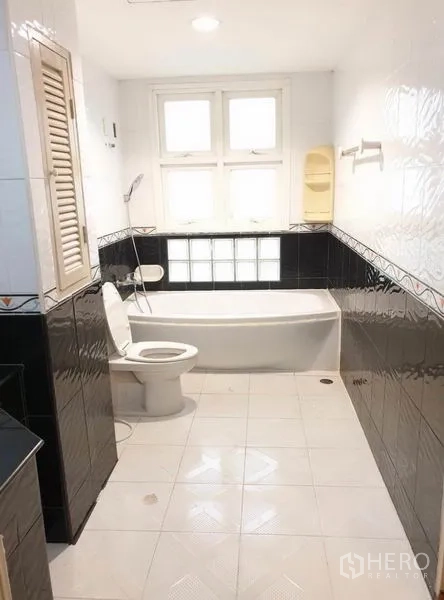 Townhouse for rent or sale in Chatuchak, Bangkok - Bathroom with bathtub under a window, toilet and black-and-white wall tiles.