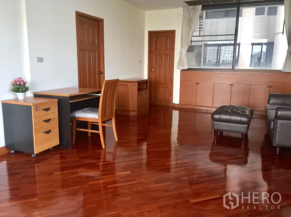 公寓 出租在Khlong Toei, Bangkok - 宽敞客厅，亮面木地板，书桌与皮沙发，临大窗