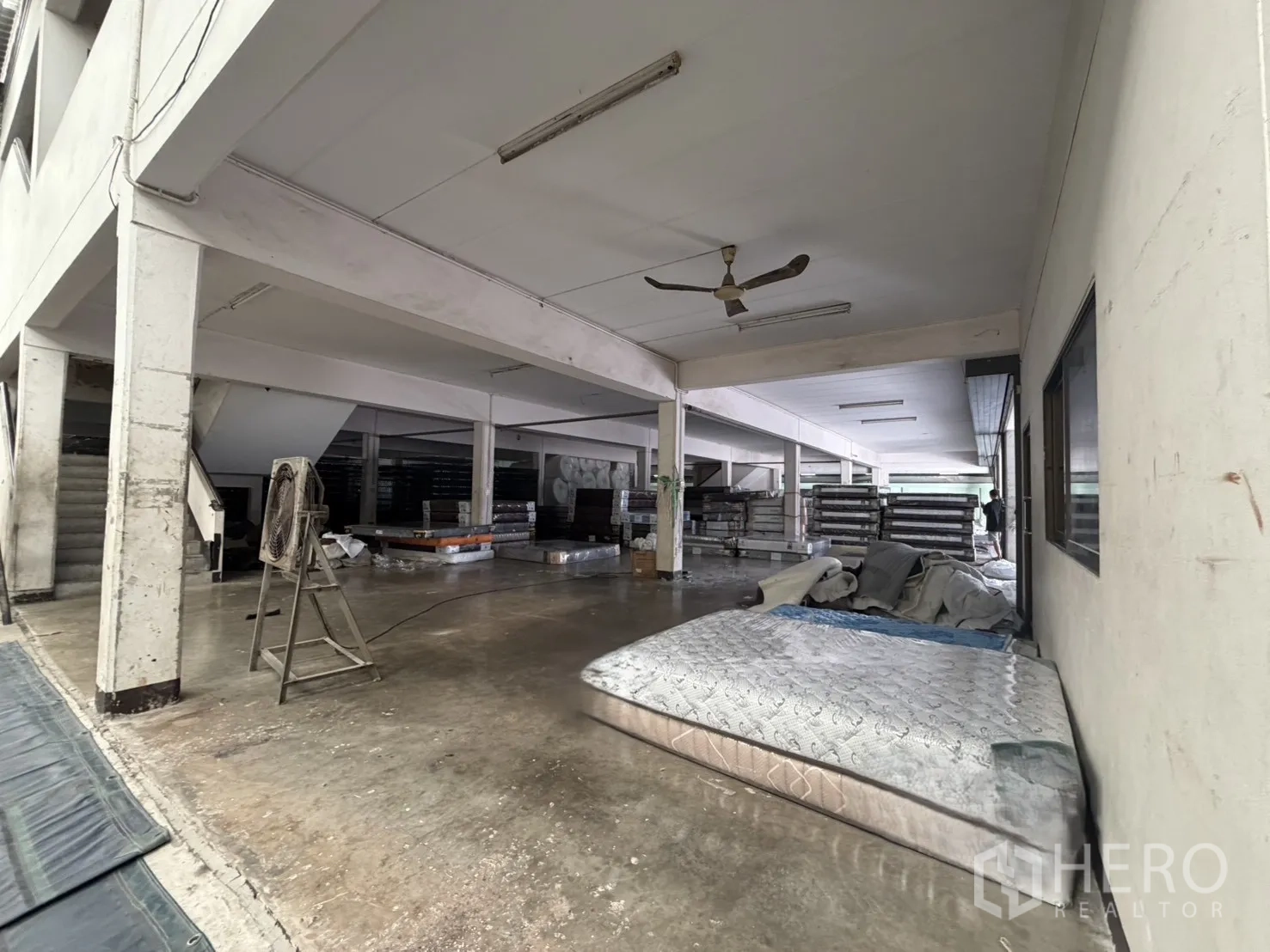 工厂 for rent or sale in Bang Bon, Bangkok - 一层作业区，有立柱、吊扇与散放材料。