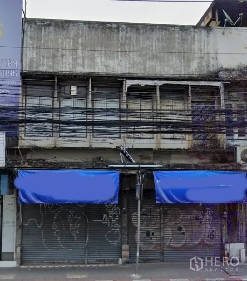 อาคารพาณิชย์ ขายในWatthana, Bangkok - อาคารพาณิชย์ติดถนน หน้าบานกว้าง มีกันสาดสีน้ำเงินและประตูม้วนโลหะ ชั้นบนมีหน้าต่างติดเหล็กดัด ในเขตวัฒนา กรุงเทพฯ