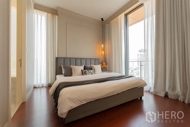 Condominium for rent in Watthana, Bangkok - Master bedroom with king bed, sheer curtains, wood floors and access to a balcony with skyline view.