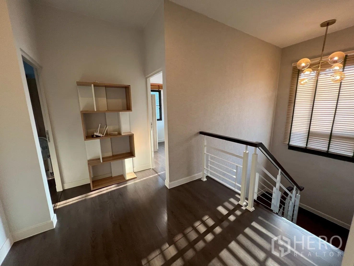 Detached House for rent in Bang Kapi, Bangkok - Upstairs landing with open shelving and staircase railing on dark wood floors.