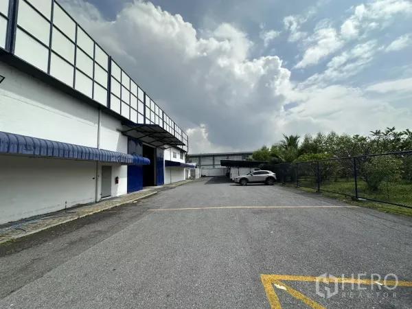 Warehouse for rent in Phra Khanong, Bangkok - Spacious driveway and parking area beside the warehouse with fence and trees, suitable for truck access.