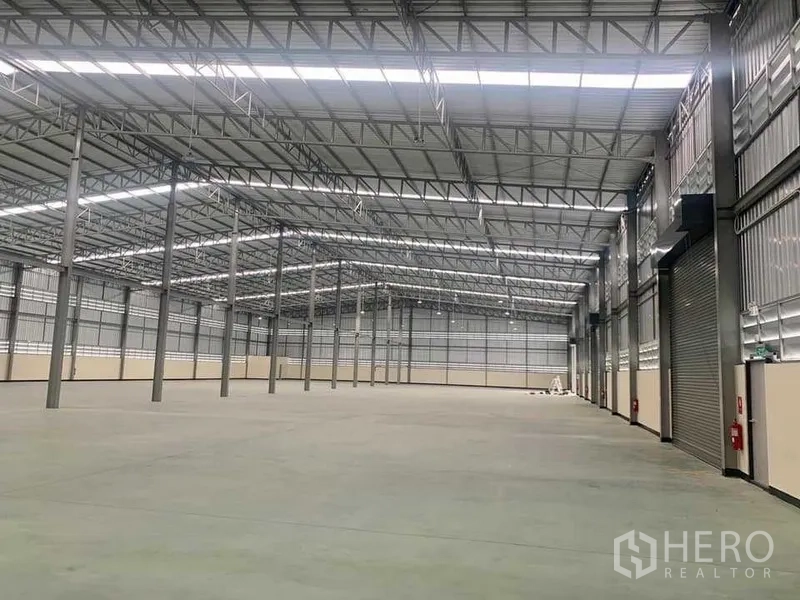 货栈 出租在Ban Bueng, Chon Buri - 宽敞仓库内部，高钢结构屋顶、平整混凝土地面与卷闸门，设消防设施。