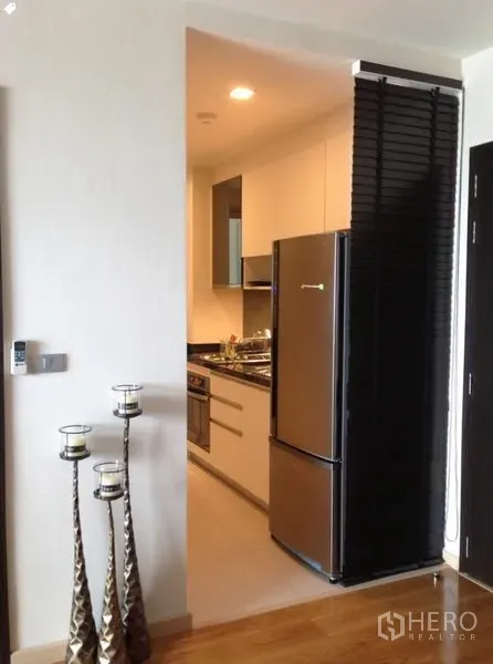 公寓 出租在Watthana, Bangkok - 紧凑走廊式厨房，配不锈钢冰箱、嵌入式炉灶和白色橱柜。