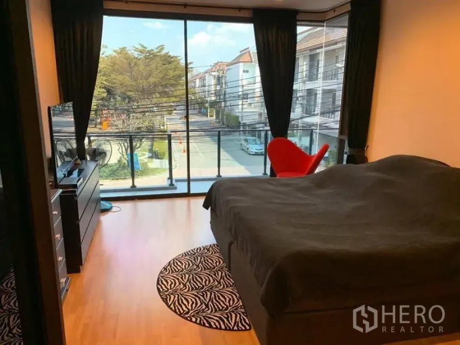 Townhouse for rent or sale in Chatuchak, Bangkok - Primary bedroom with floor‑to‑ceiling glass, balcony, wood floors and street view.