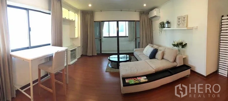 Condominium for rent or sale in Din Daeng, Bangkok - Living area with sectional sofa, round coffee table and sliding glass doors to a balcony.