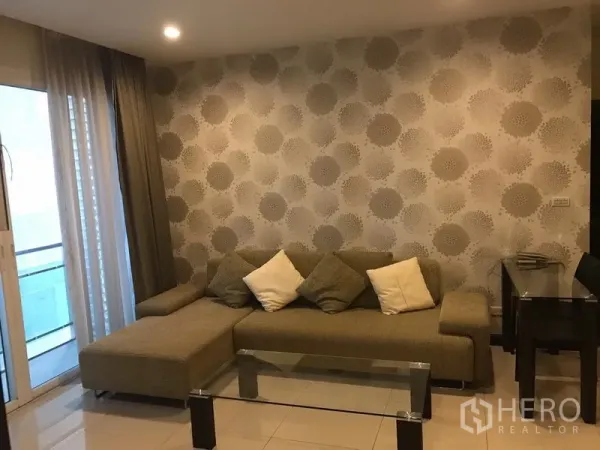 Condominium for rent in Watthana, Bangkok - Living room with L-shaped sofa, patterned feature wall, glass coffee table and sliding door to balcony.