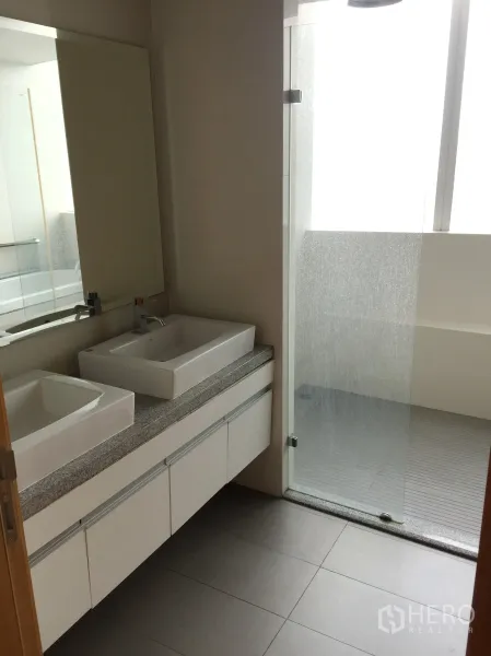 Condominium for rent in Khlong Toei, Bangkok - Modern bathroom featuring a double vanity, large mirror and glass-enclosed shower.