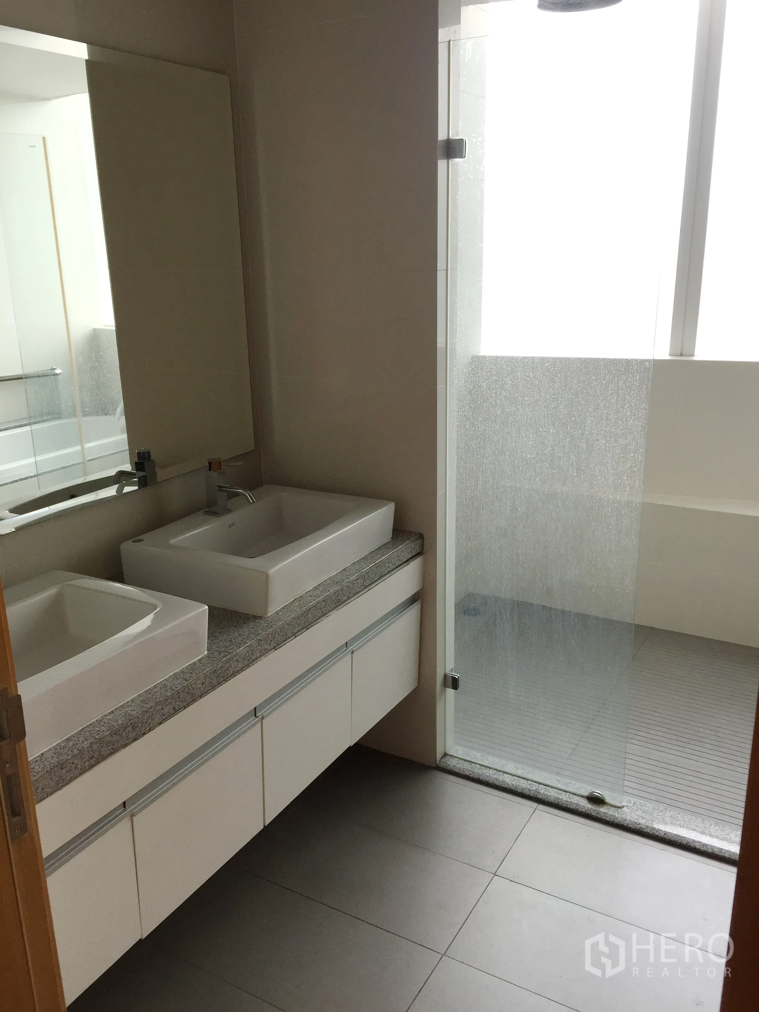 Condominium for rent in Khlong Toei, Bangkok - Modern bathroom featuring a double vanity, large mirror and glass-enclosed shower.
