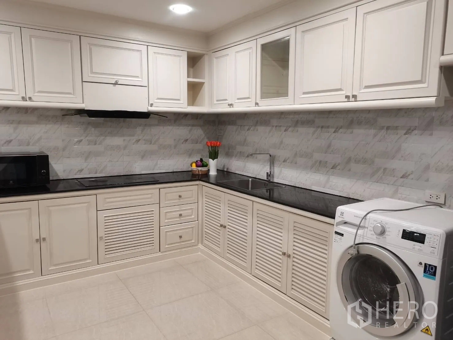 公寓 for rent in Watthana, Bangkok - 白色L形厨房，电磁炉、抽油烟机、水槽、微波炉和滚筒洗衣机。