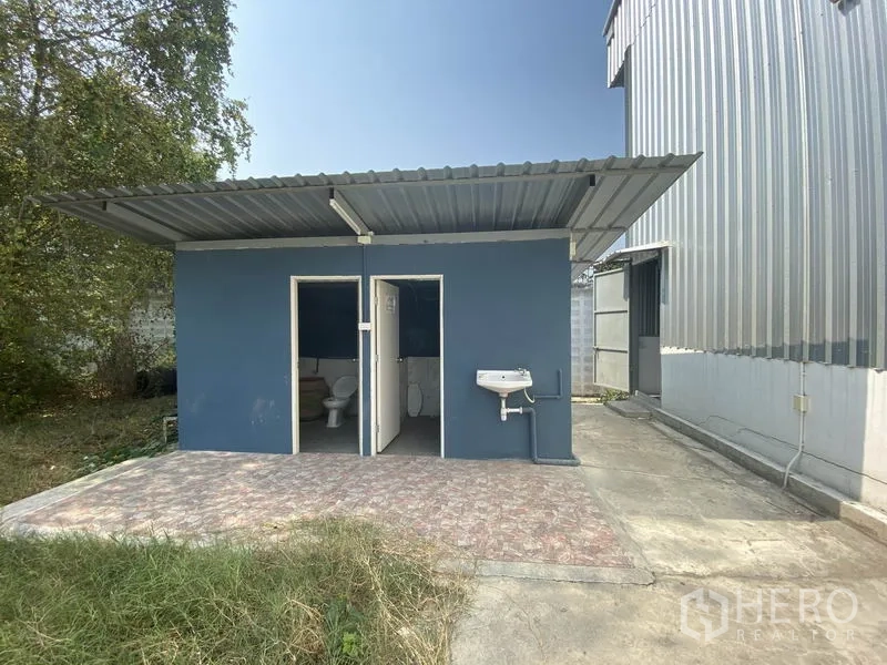 货栈 出租在Prawet, Bangkok - 仓库旁独立蓝色卫生间建筑，两个厕间并配有室外洗手盆。