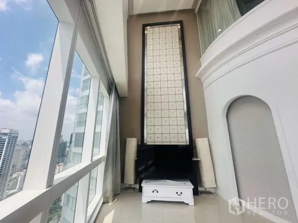 Condominium for rent or sale in Khlong Toei, Bangkok - Corner lounge with towering feature wall, TV console and panoramic city views through full-height glass windows.