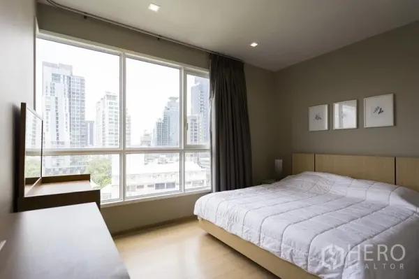 Condominium for rent in Watthana, Bangkok - Bedroom with large windows, city skyline views and a queen bed with light wood furniture.