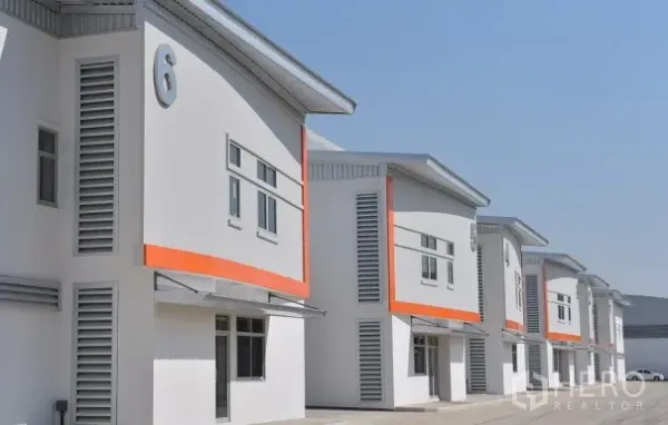 Factory for rent in Phra Nakhon Si Ayutthaya - Modern row of factory units in a secured compound with numbered facades, orange accents and wide driveway.