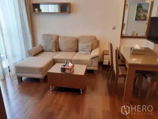 公寓 出租在Watthana, Bangkok - 木地板客厅，米色转角沙发、茶几与大窗帘，毗邻餐桌。