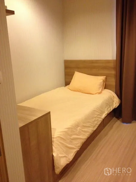 Condominium for rent in Huai Khwang, Bangkok - Cozy secondary bedroom with single bed, wood headboard, soft lighting, and blackout curtains.