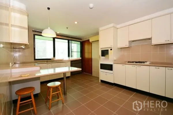Apartment for rent in Khlong Toei, Bangkok - Separate kitchen with tiled floors, ample cabinetry, built-in oven, gas hob and breakfast counter with stools.