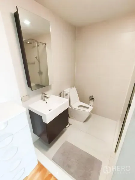 Condominium for rent in Khlong Toei, Bangkok - Bright bathroom with wall-hung vanity, mirror cabinet and modern toilet on light tiles.