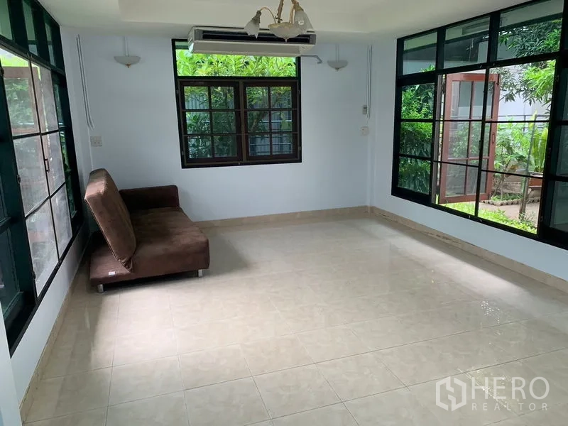 Detached House for rent in Khlong Toei, Bangkok - Glass-wrapped family room with tiled floor, garden views and a sofa.