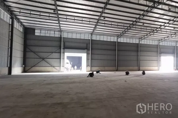 Warehouse for rent in Bang Bo, Samut Prakan - Large empty warehouse hall with concrete flooring and bright openings from roller doors at both ends.