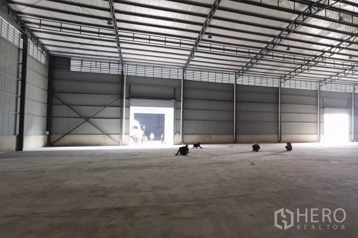 Warehouse for rent in Bang Bo, Samut Prakan - Large empty warehouse hall with concrete flooring and bright openings from roller doors at both ends.