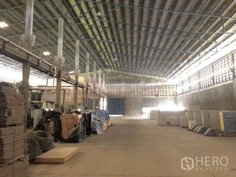 Factory for rent in Bang Bua Thong, Nonthaburi - Warehouse zone with stacked materials, a wide central aisle, and a roller door.