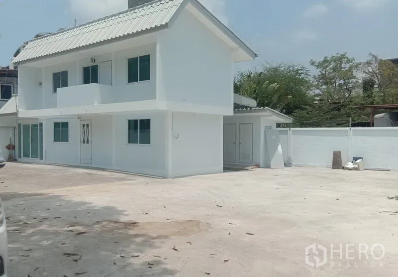 Home Office for rent in Khlong Toei, Bangkok - Two-storey white home office with a large concrete yard and perimeter wall in Khlong Toei, ideal for parking.