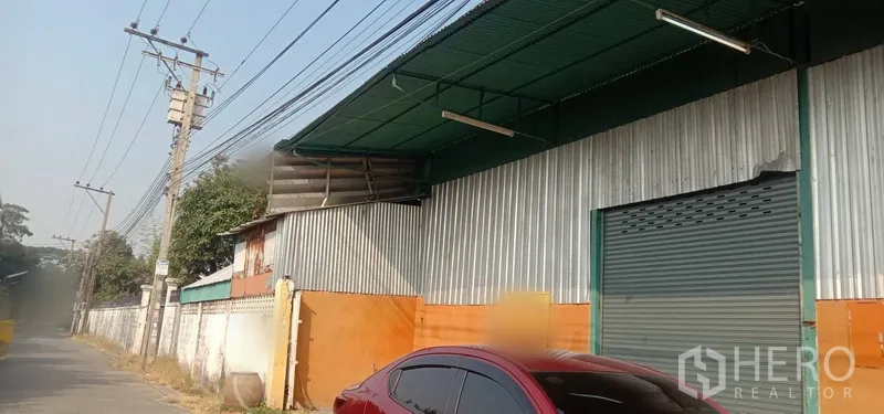 Warehouse for rent in Bueng Kum, Bangkok - Street-side warehouse exterior with corrugated metal cladding, green awning and a large roll-up door in Bueng Kum, Bangkok.