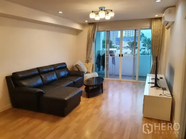 公寓 出租在Watthana, Bangkok - 宽敞客厅，黑色皮质转角沙发、电视柜，落地推拉门通向阳台。