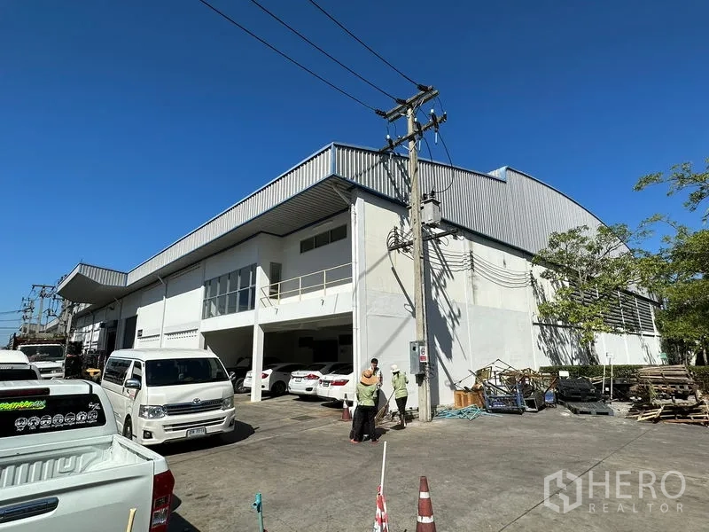 โรงงาน ให้เช่าในSi Racha, Chon Buri - มุมมองภายนอกอาคารโรงงานสีขาวหลังคาเมทัลชีท มีที่จอดรถและเสาไฟฟ้าใต้ท้องฟ้าโปร่งในศรีราชา