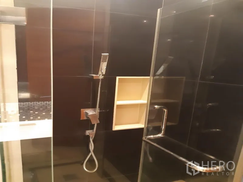 Condominium for rent or sale in Khlong Toei, Bangkok - Walk-in glass shower with black tiles, handheld showerhead and built-in shelf.